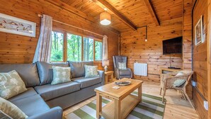 L’intérieur chaleureux d’un chalet avec un canapé, un fauteuil, une table basse en bois et un téléviseur fixé au mur.