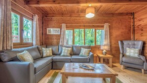 L’intérieur d’un chalet en bois, avec un canapé d’angle, un fauteuil, une table et une lampe.