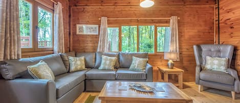 A wooden cabin interior with a sectional sofa, a chair, a table, and a lamp.