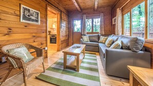 L’intérieur d’un chalet accueillant, avec un plafond en bois, un canapé, un fauteuil en osier, une table à manger et un coin cuisine.