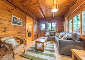 A cozy cabin interior with a wooden ceiling, a sofa, a wicker chair, a dining table, and a kitchen area. - Woodland Hawthorn Lodge (Ellesmere)