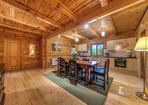 A wooden cabin interior with a dining table, chairs, a kitchen area, and a window. - Woodland Hawthorn Lodge (Ellesmere)