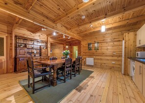 A wooden cabin interior with a dining area, kitchen, and a visible door leading outside. - Woodland Hawthorn Lodge (Ellesmere)