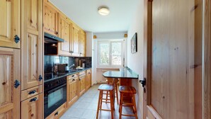 Une cuisine avec des meubles de rangement en bois, un poêle noir et une fenêtre donnant sur un paysage verdoyant.