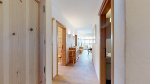 Um corredor estreito com pisos de madeira e portas que dão para uma área de cozinha com mesa e cadeiras.