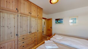 Une chambre avec deux lits simples, des armoires en bois et deux œuvres d’art encadrées accrochées au mur.