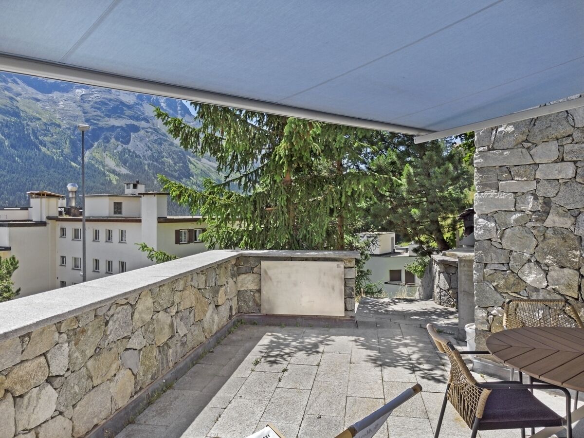 A rooftop terrace with stone walls, a table, and chairs.