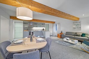 Eine moderne Küche mit integrierten Geräten, ein Essbereich mit rundem Tisch und Stühlen sowie ein Wohnbereich mit einer Couch und einem Couchtisch.