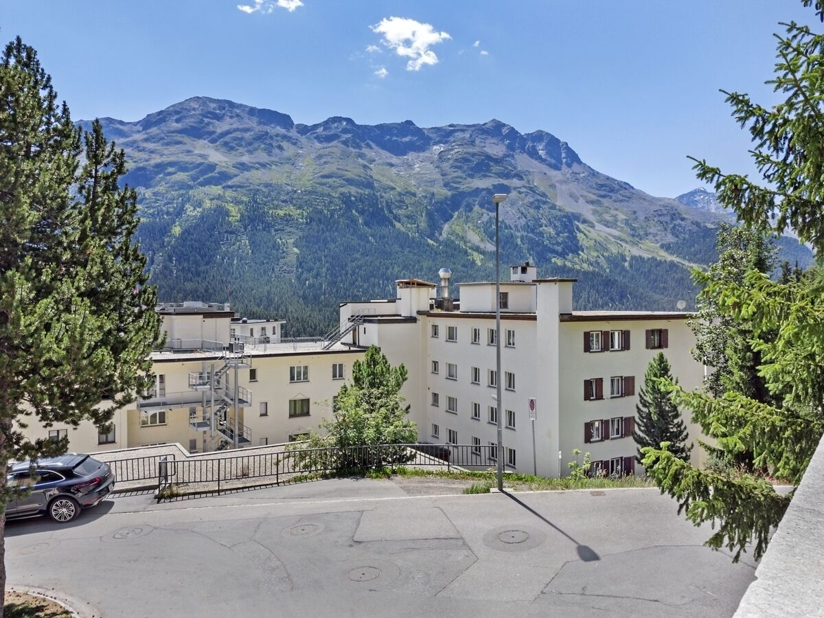 A building with multiple floors, a parking area, and a mountainous backdrop.