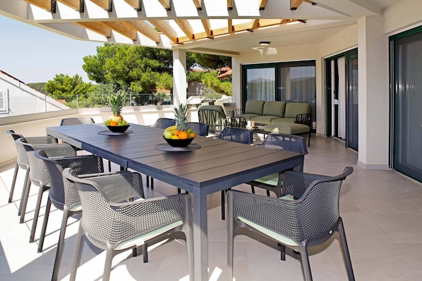 A covered outdoor dining area with a table and chairs, a bowl of fruit, and a view of the surrounding landscape.