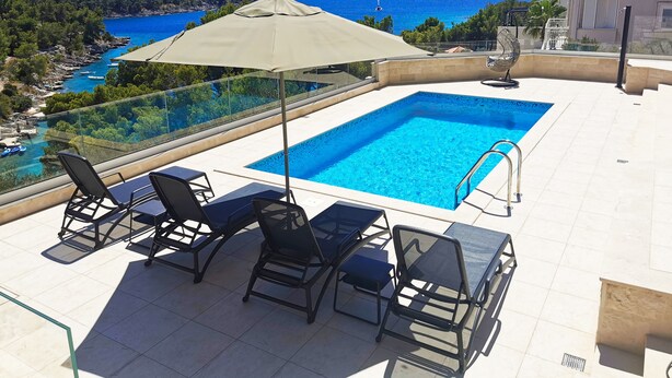 A rooftop pool with clear blue water, surrounded by lounge chairs and an umbrella. - Beachfront villa Senses for 12 in Milna (Milna)