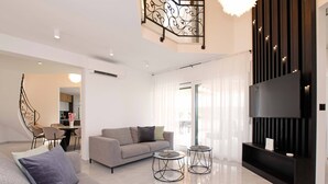 A modern living room with a sofa, two coffee tables, a TV, and a dining area in the background. - Beachfront villa Senses for 12 in Milna (Milna)