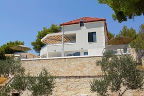 Un bâtiment moderne à deux étages, doté d’une façade en pierre, d’un toit recouvert de tuiles rouges et d’un balcon agrémenté d’une pergola.