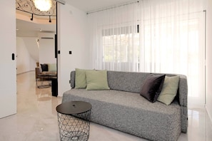 A modern living room with a grey sofa, a round black coffee table, and a dining area in the background.