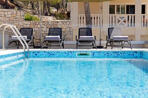 Une piscine bordée d’un muret en pierre et dotée d’un espace détente abrité, avec des chaises longues.