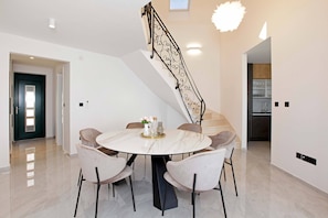 A modern dining area with a marble table, six chairs, and a decorative staircase with a metal railing.