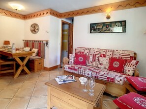 A cozy living room with a wooden table, a sofa with red cushions, and a wall-mounted picture frame.