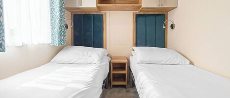 A double room with two beds, a wooden shelf above, and a small bedside table.