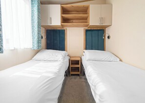 Een tweepersoonskamer met twee bedden, een houten plank erboven en een klein nachtkastje.