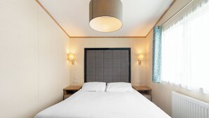 Habitación de hotel con una cama grande, dos mesitas de noche, un cabecero y una ventana con cortinas.