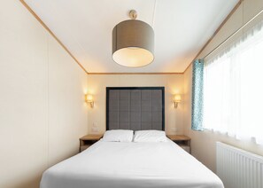 Een hotelkamer met een groot bed, twee nachtkastjes, een hoofdbord en een raam met gordijnen.