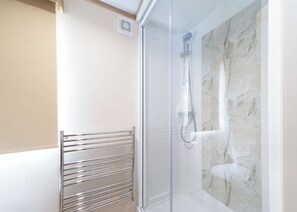 Een moderne douche met een glazen deur, een marmeren wand en een metalen handdoekhouder.