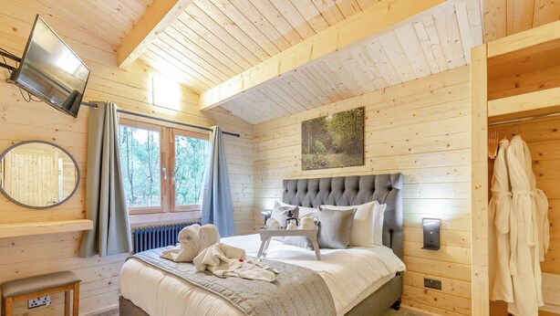 A wooden cabin bedroom with a bed, a mirror, a window, a picture on the wall, and a robe rack. - 1 bedroom accommodation in Freehay, Cheadle (Freehay, Cheadle)
