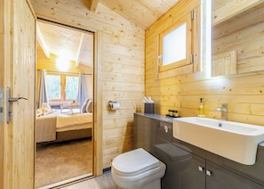 L’intérieur d’un chalet en bois comprend un lit, une salle de bain avec un lavabo et des toilettes, ainsi qu’une fenêtre.