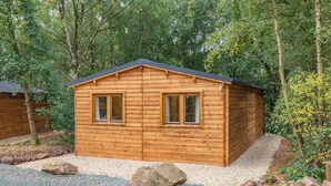 A wooden cabin with two windows, surrounded by trees and gravel. - 1 bedroom accommodation in Freehay, Cheadle (Freehay, Cheadle)