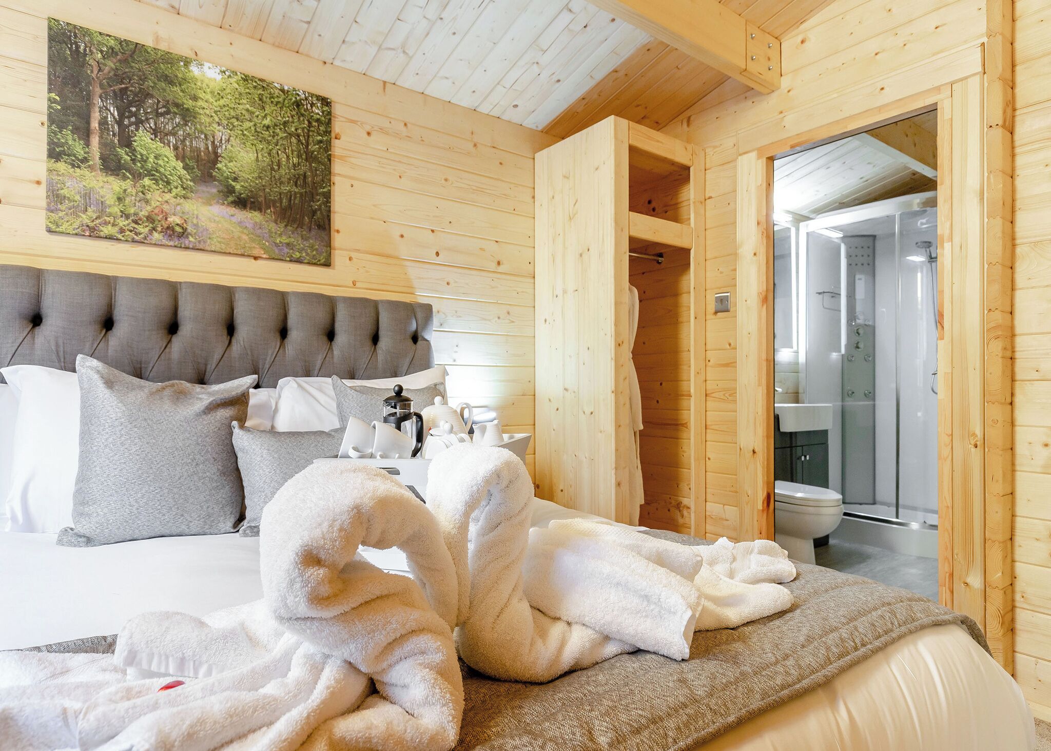 A wooden cabin bedroom with a bed, pillows, a painting, and a bathroom with a shower.