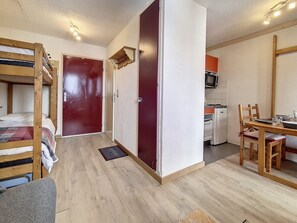 A compact room with a bunk bed, a kitchenette, a dining table with chairs, and a red door. - Cozy studio at ski slopes with balcony (Les Menuires)
