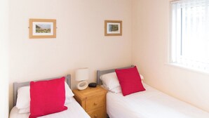 Une chambre double avec deux lits, chacun agrémenté d’un oreiller rouge, une table de chevet avec une lampe et des tableaux encadrés accrochés au mur.