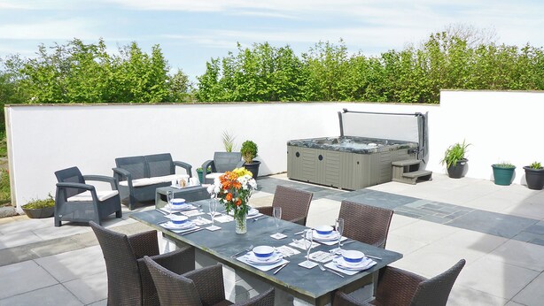 Eine Terrassensitzgruppe im Freien mit Esstisch, Korbstühlen, einem Whirlpool und Kübelpflanzen.