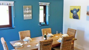 Ein Esszimmer mit einem für sechs Personen gedeckten Tisch, Korbstühlen und einer blauen Wand mit Spiegel und Kunstwerken.