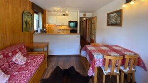 Une pièce confortable avec un canapé, une table à manger et des chaises, un coin cuisine et un couloir menant à une autre pièce.