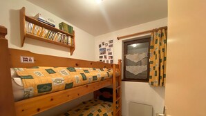 Une petite pièce avec deux lits superposés, une bibliothèque, une fenêtre avec des rideaux et un radiateur.