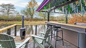 Eine Terrasse mit Grill, Barhocker und Blick auf ein Gewässer.