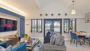 Ein modernes Wohnzimmer mit Flachbildfernseher, grauem Sofa, Couchtisch und Essbereich mit Tisch für vier Personen.