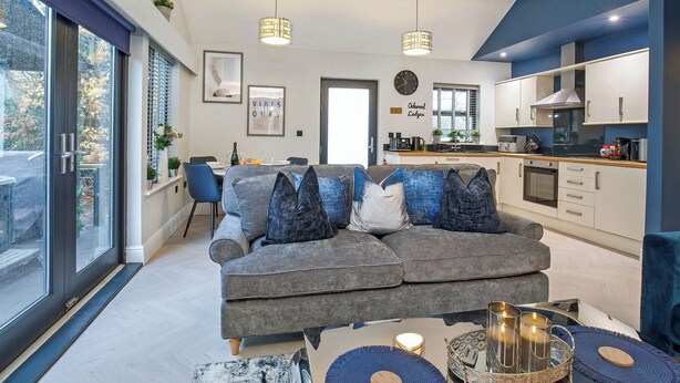 Ein modernes Wohnzimmer mit grauem Sofa, Essbereich, Küche und großen Fenstern.