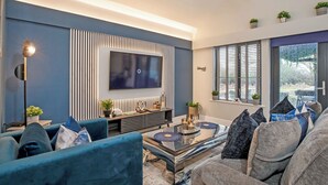 Ein modernes Wohnzimmer mit einem großen Flachbildfernseher an der Wand, einer Sofagarnitur, einem Couchtisch und einer Stehlampe.