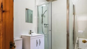Une salle de bain comprenant des toilettes, un lavabo, un miroir et une douche séparée par une paroi en verre.