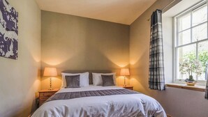 Une chambre à coucher avec un grand lit, deux lampes de chevet, une fenêtre avec des rideaux et un mur orné d’un motif floral.