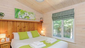 A wooden-paneled bedroom with a bed, bedside lamps, a window with a view, and a painting on the wall. - Luxurious and contemporary lodge with stunning countryside views. (Ashover)