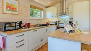 A modern kitchen with wooden cabinets, a built-in microwave, a kettle, and a window with a view of greenery. - Luxurious and contemporary lodge with stunning countryside views. (Ashover)