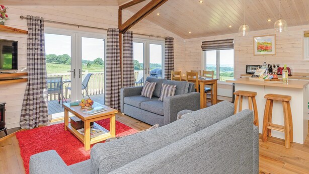 A spacious living area with a sofa, a table, and a kitchen area with a bar. - Luxurious and contemporary lodge with stunning countryside views. (Ashover)