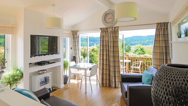 A living room with a television, a fireplace, a dining area, and a balcony with a view of the countryside. - Lodge with one king-size double with TV. (Newby Bridge, Lake Windermere)