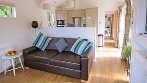 A modern living room with a brown leather sofa, a small white table with fruit, and a kitchen in the background. - Lodge with one king-size double with TV. (Newby Bridge, Lake Windermere)