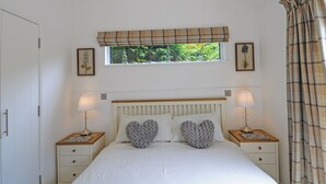 A bedroom with a bed, two bedside tables with lamps, a window with a view of greenery, and a door. - Lodge with one king-size double with TV. (Newby Bridge, Lake Windermere)