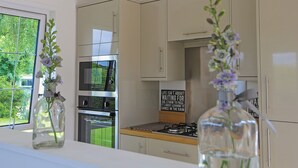 A modern kitchen with stainless steel appliances, beige cabinetry, and a view of greenery outside. - Lodge with one king-size double with TV. (Newby Bridge, Lake Windermere)