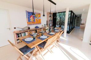 A dining area with a long wooden table set for six, surrounded by chairs with blue cushions.